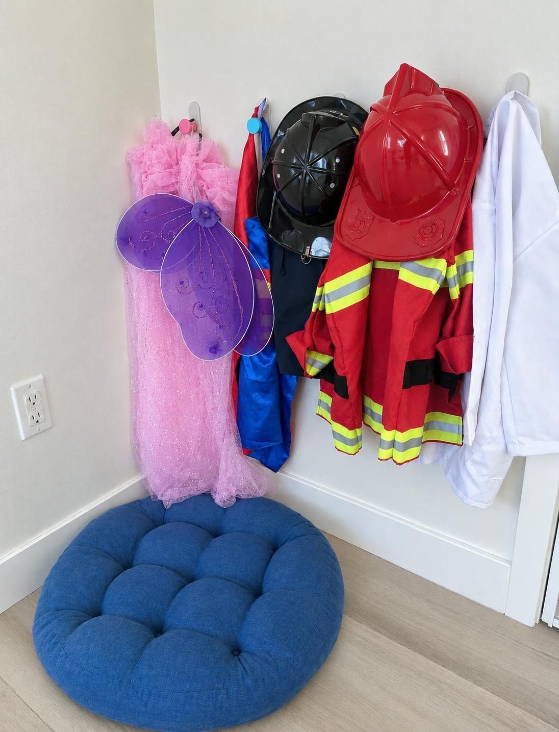 Child costumes and hats hanging on wall hooks above a blue floor cushion