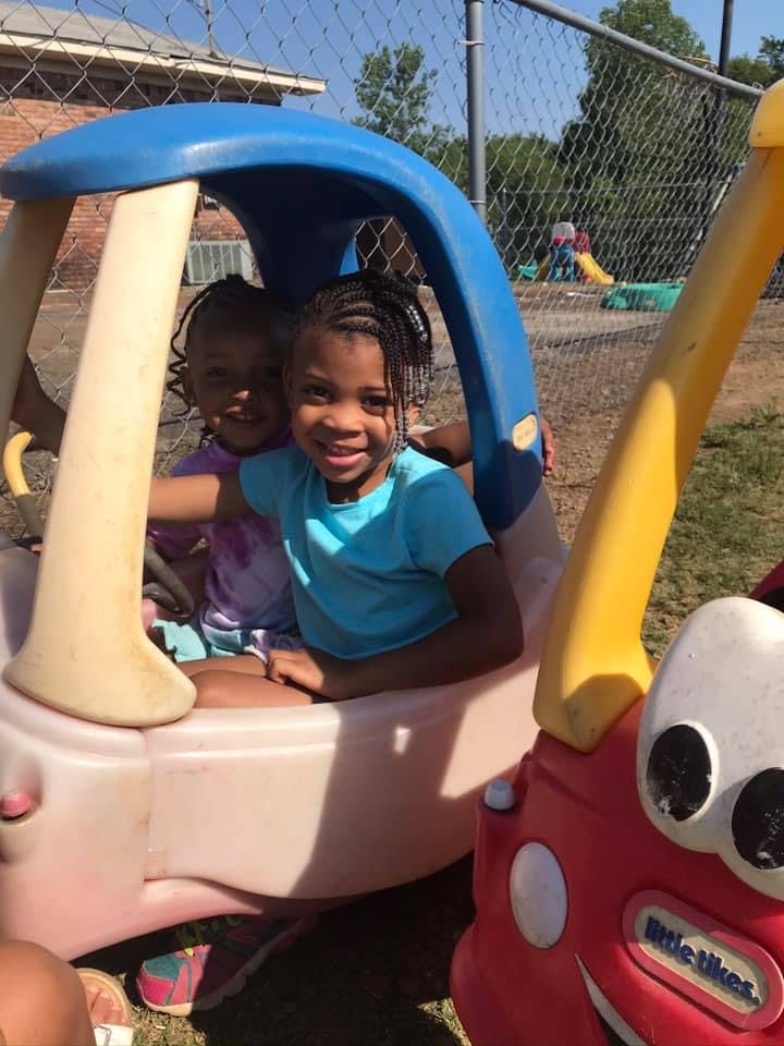 Two children sitting in a toy car on a playground