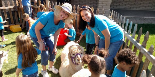Two people and children interacting with a llama in a fenced area