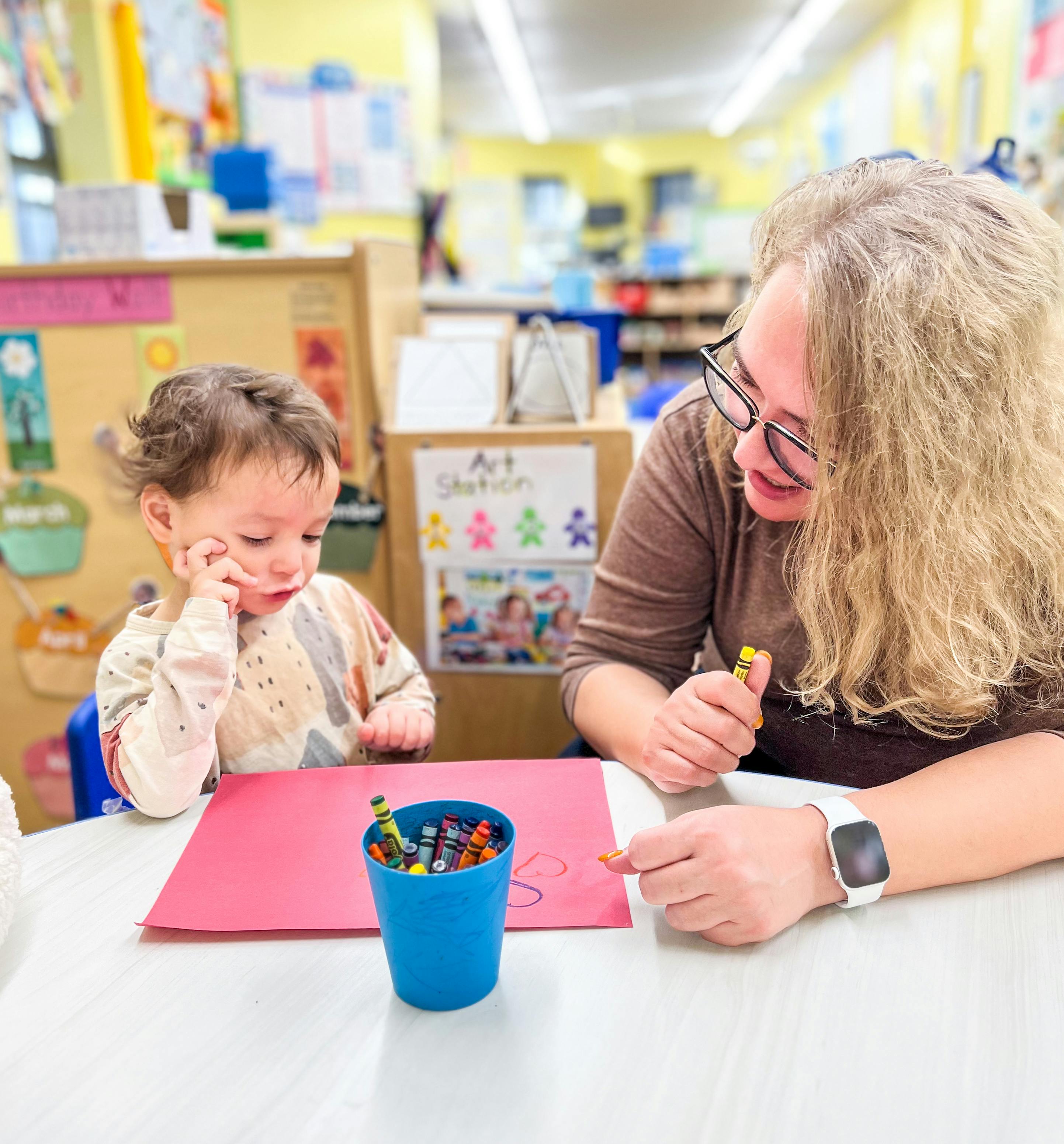 Adult and child drawing with crayons in a classroom