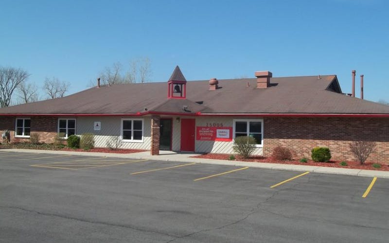 Single story building with a red door, small bell tower, and parking lot in front