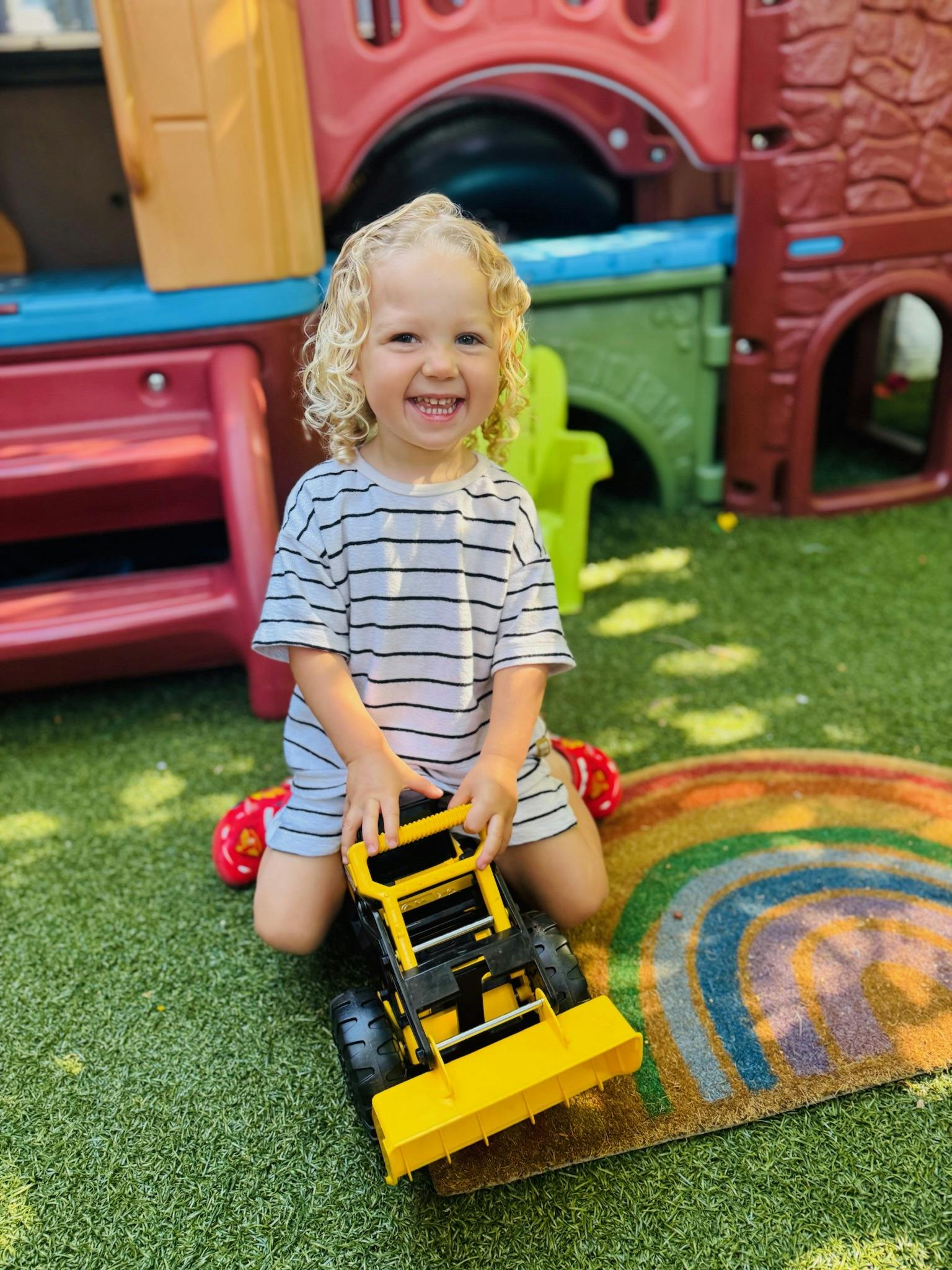Child kneeling on grass with a yellow toy construction vehicle