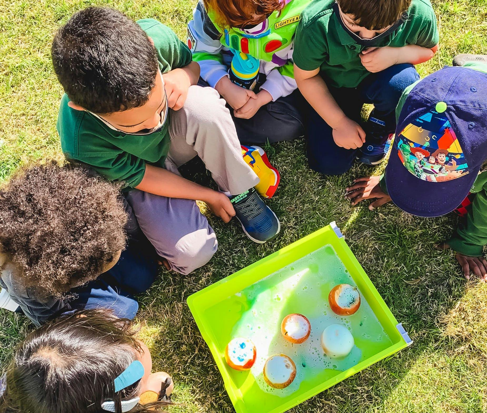 Children gathered around a tray with floating objects on grass