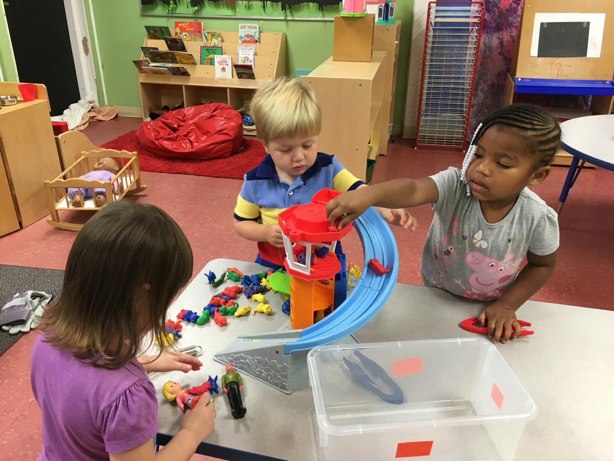 Three children playing with toys at a table in a classroom
