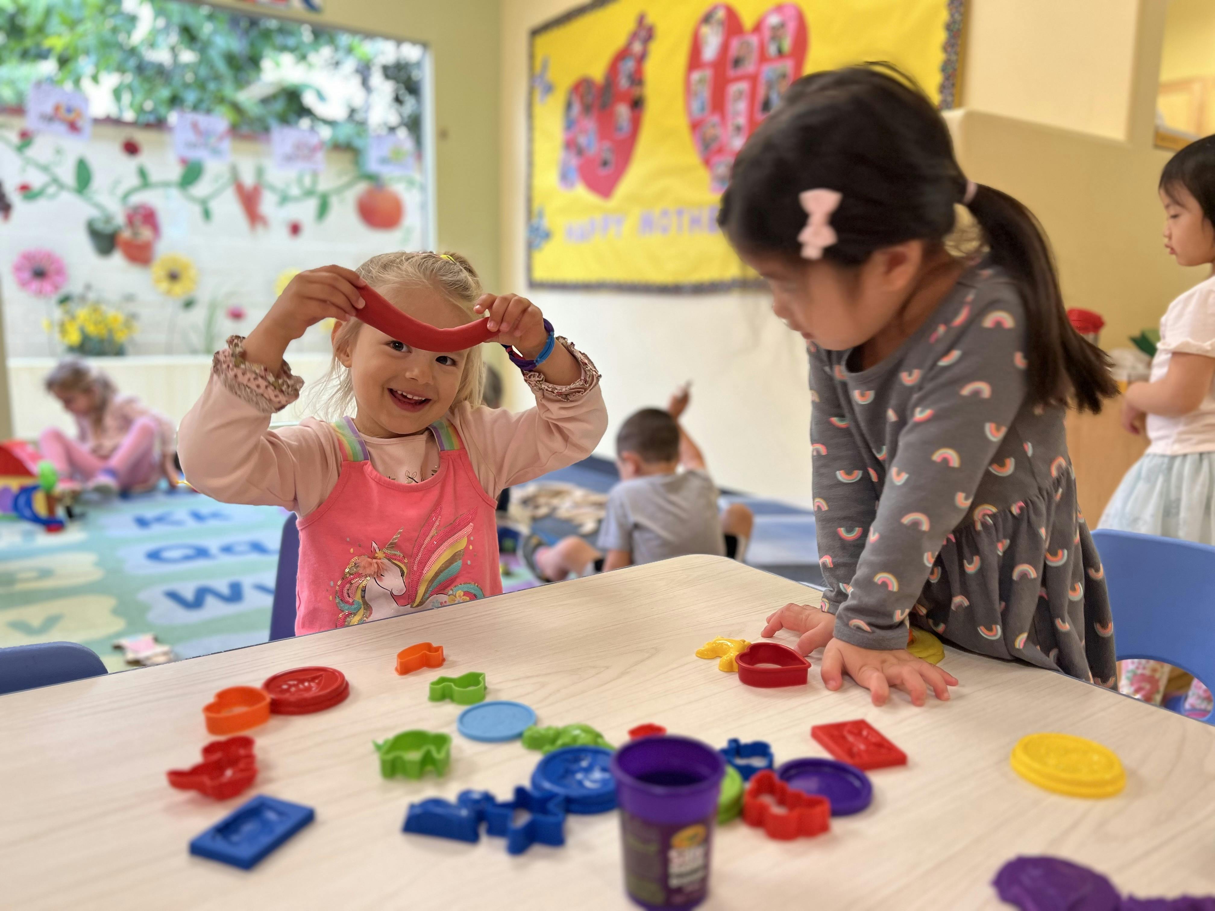 Two children playing with colorful shapes at a table in a classroom