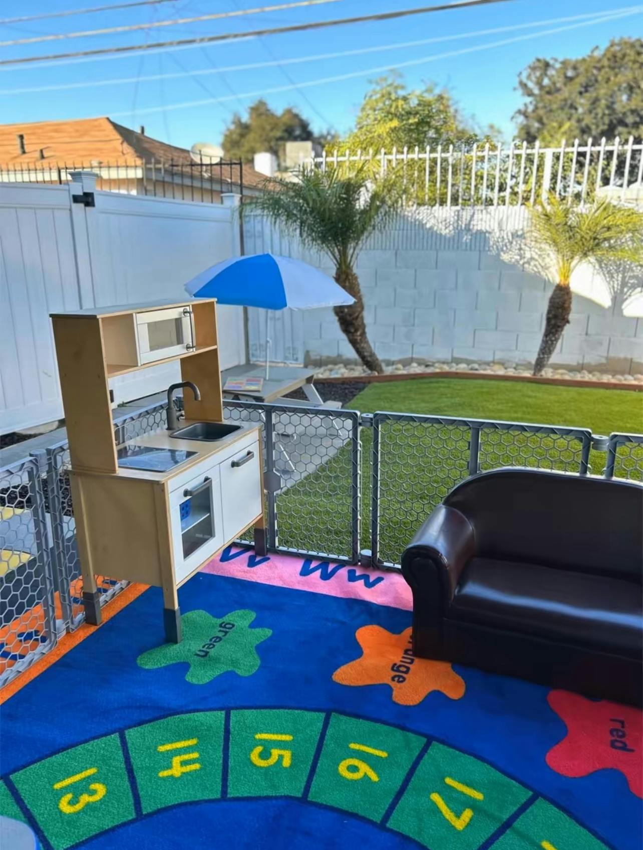Play kitchen and small couch on a colorful rug in an outdoor play area