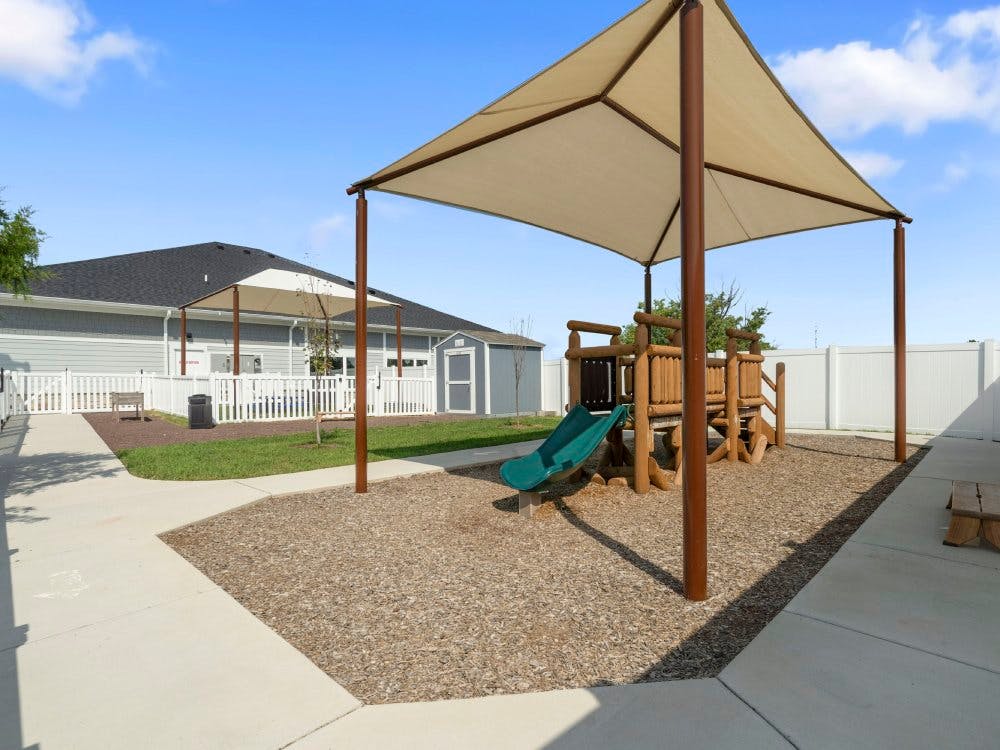 Outdoor playground with a wooden play structure, green slide, and shade canopy