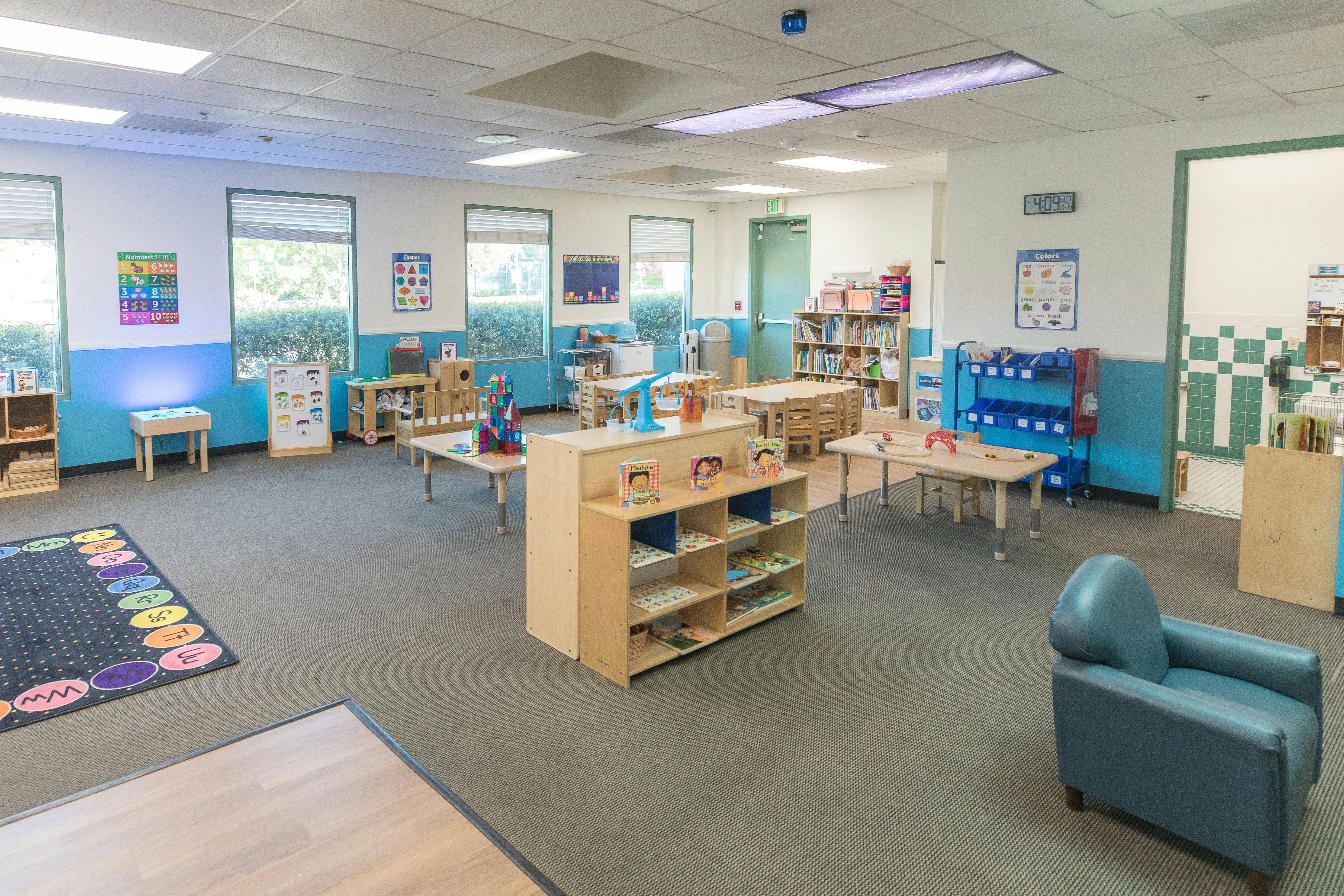 Empty classroom with small tables, chairs, and shelves