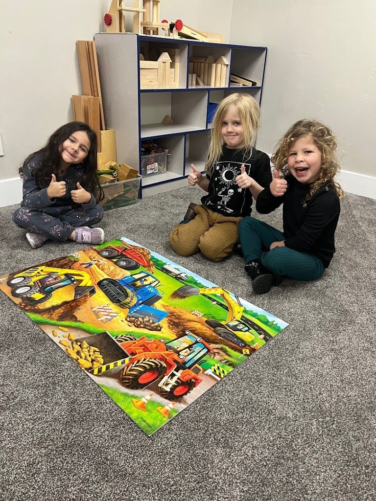 Three children giving thumbs up next to a construction puzzle