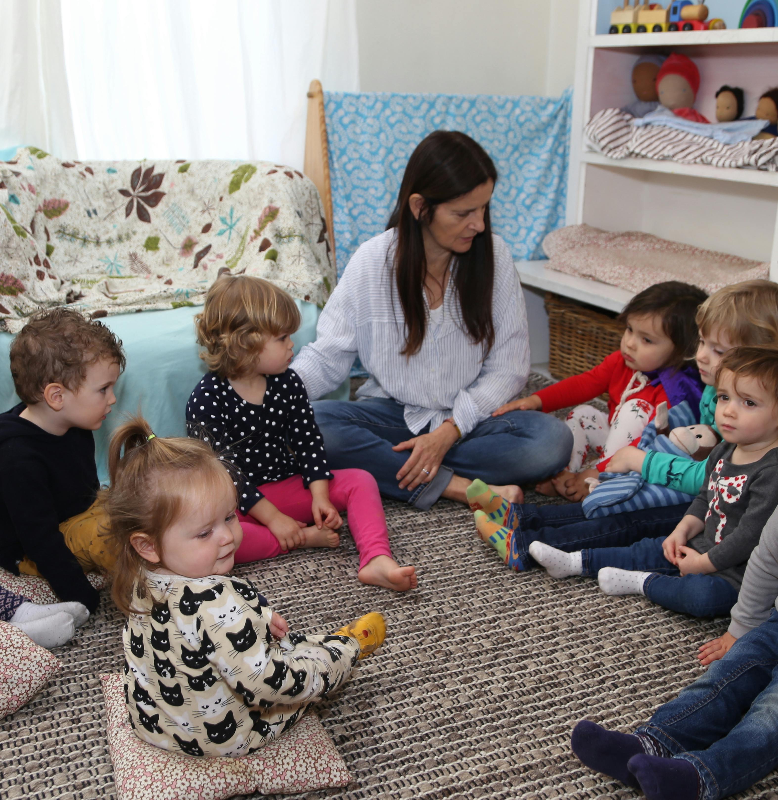 Person sitting on floor with several children in a classroom