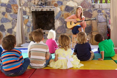 Person playing guitar for a group of children sitting on the floor