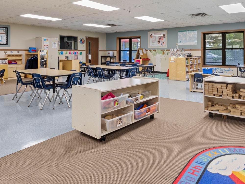 Empty classroom with tables and chairs, shelves of toys and learning materials