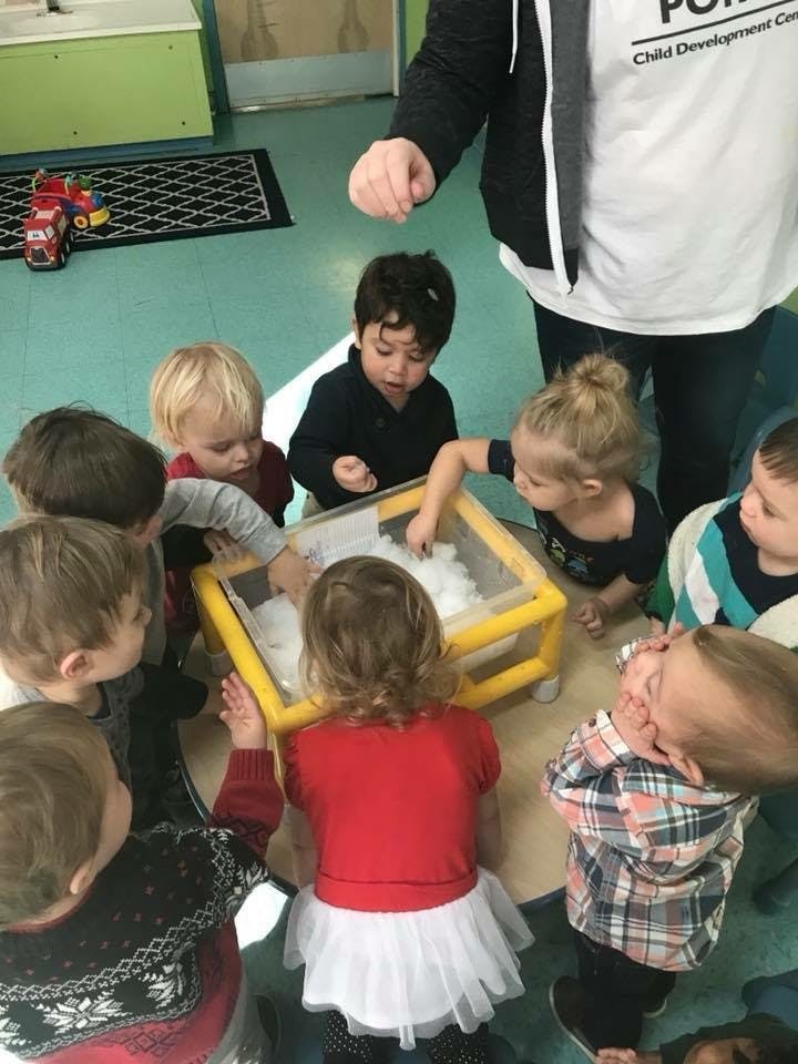 Children gathered around a sensory bin with a person standing nearby
