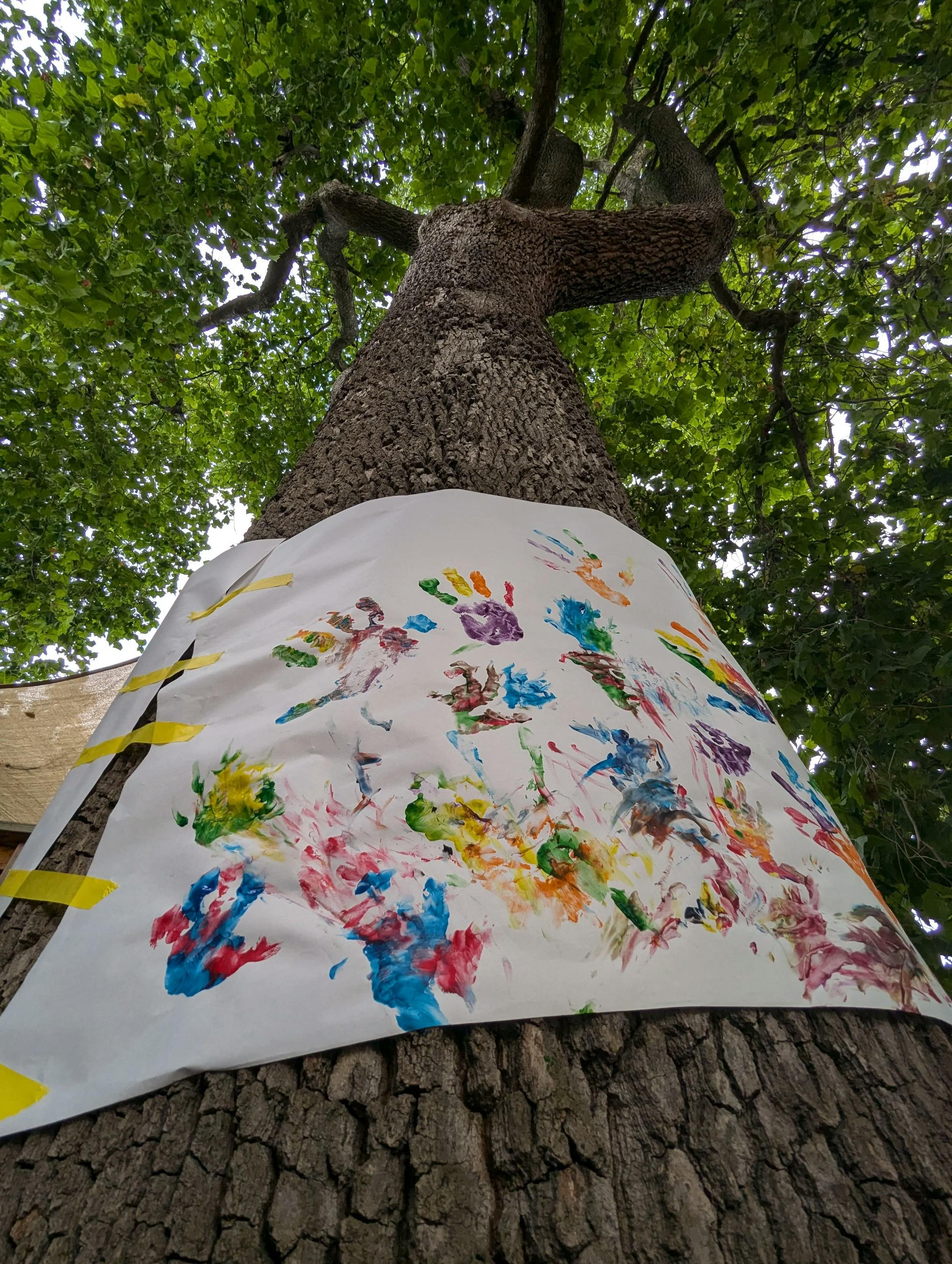 White paper with colorful handprints taped to a tree trunk