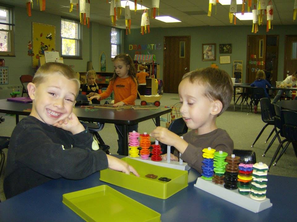 Two children playing with stacking toys at a table in a classroom