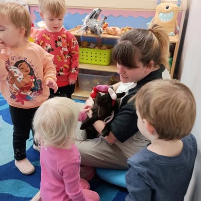 A person holding a small goat while children gather around to pet it