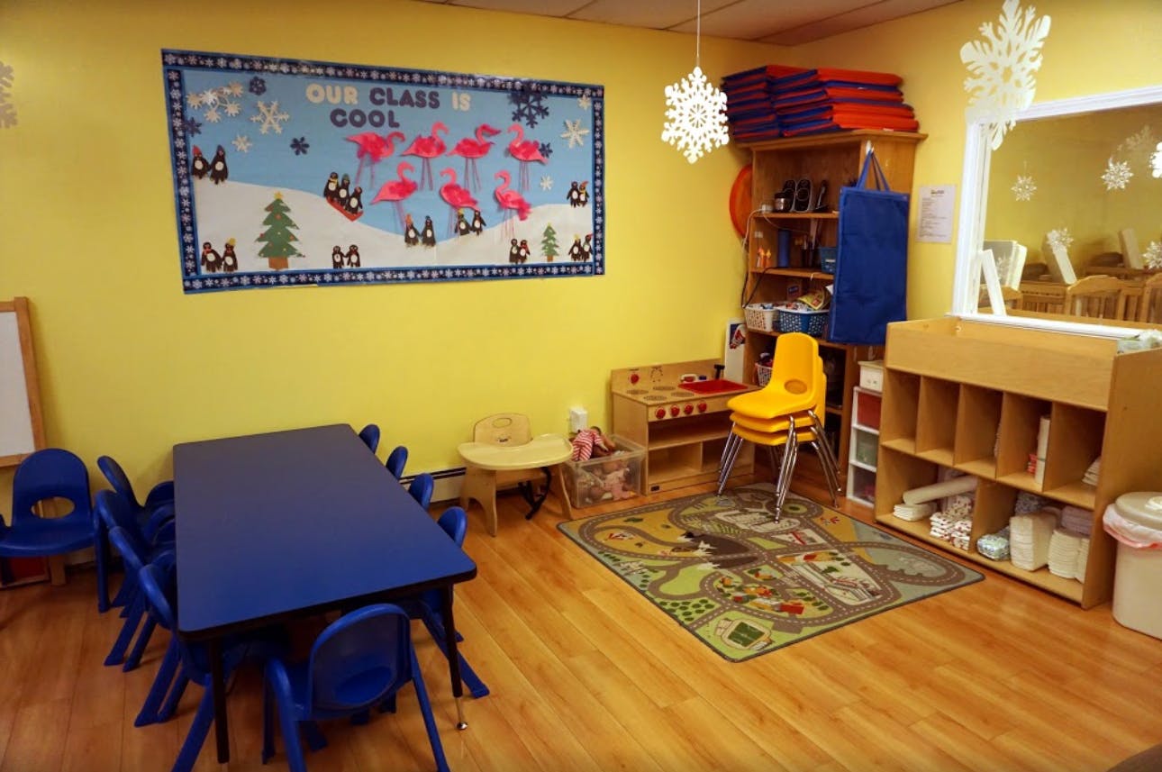 Classroom with blue tables and chairs, play kitchen, and colorful rug