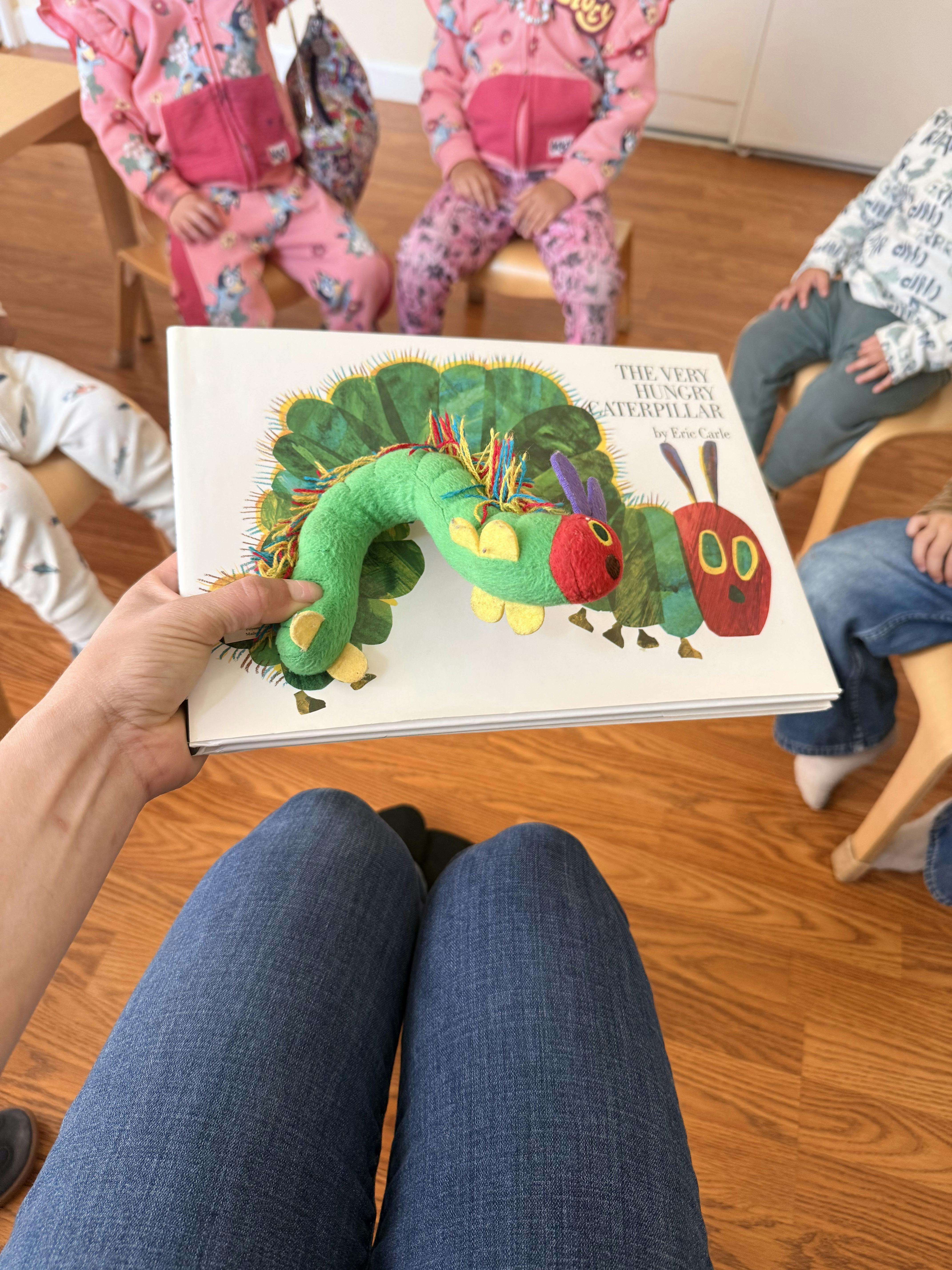 Person holding The Very Hungry Caterpillar book and plush toy for children