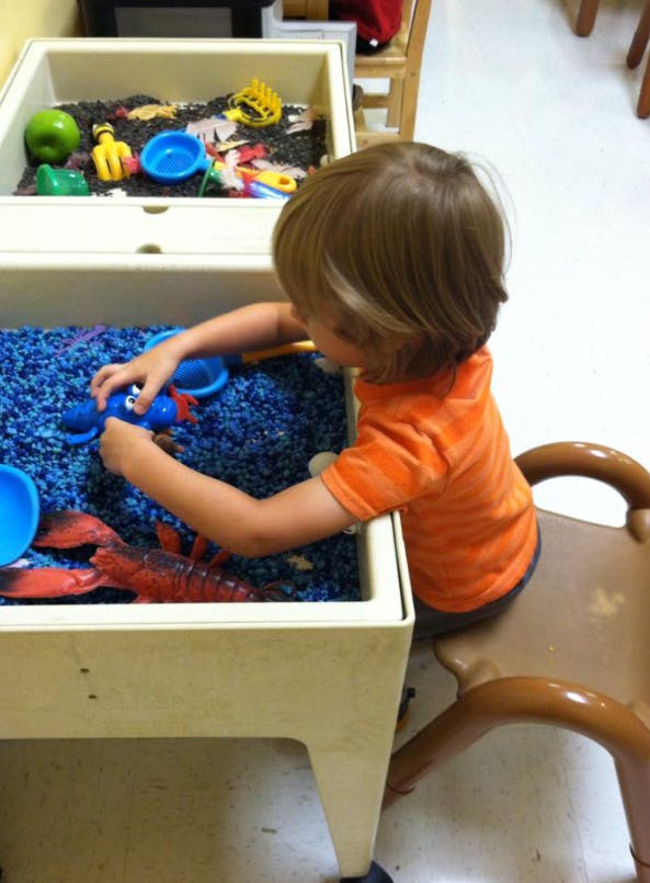 Child playing with blue beads and toys in a sensory table