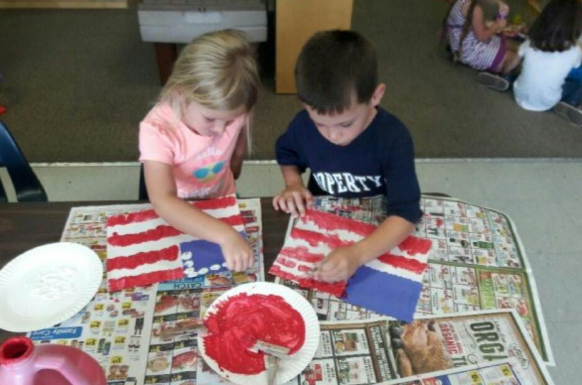 Two children making crafts with red and white stripes and blue squares