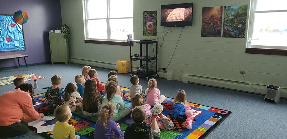 Adult and children sitting on a colorful rug in a classroom