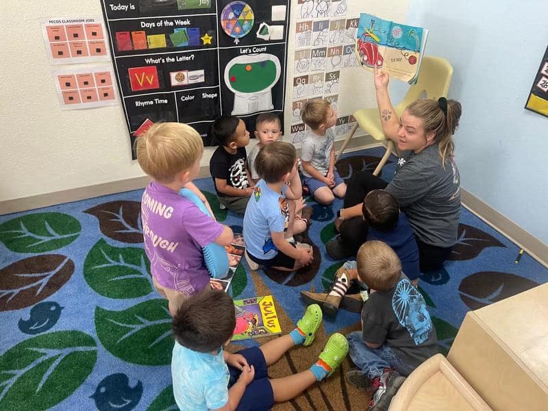 Adult reading a book to a group of children sitting on a rug