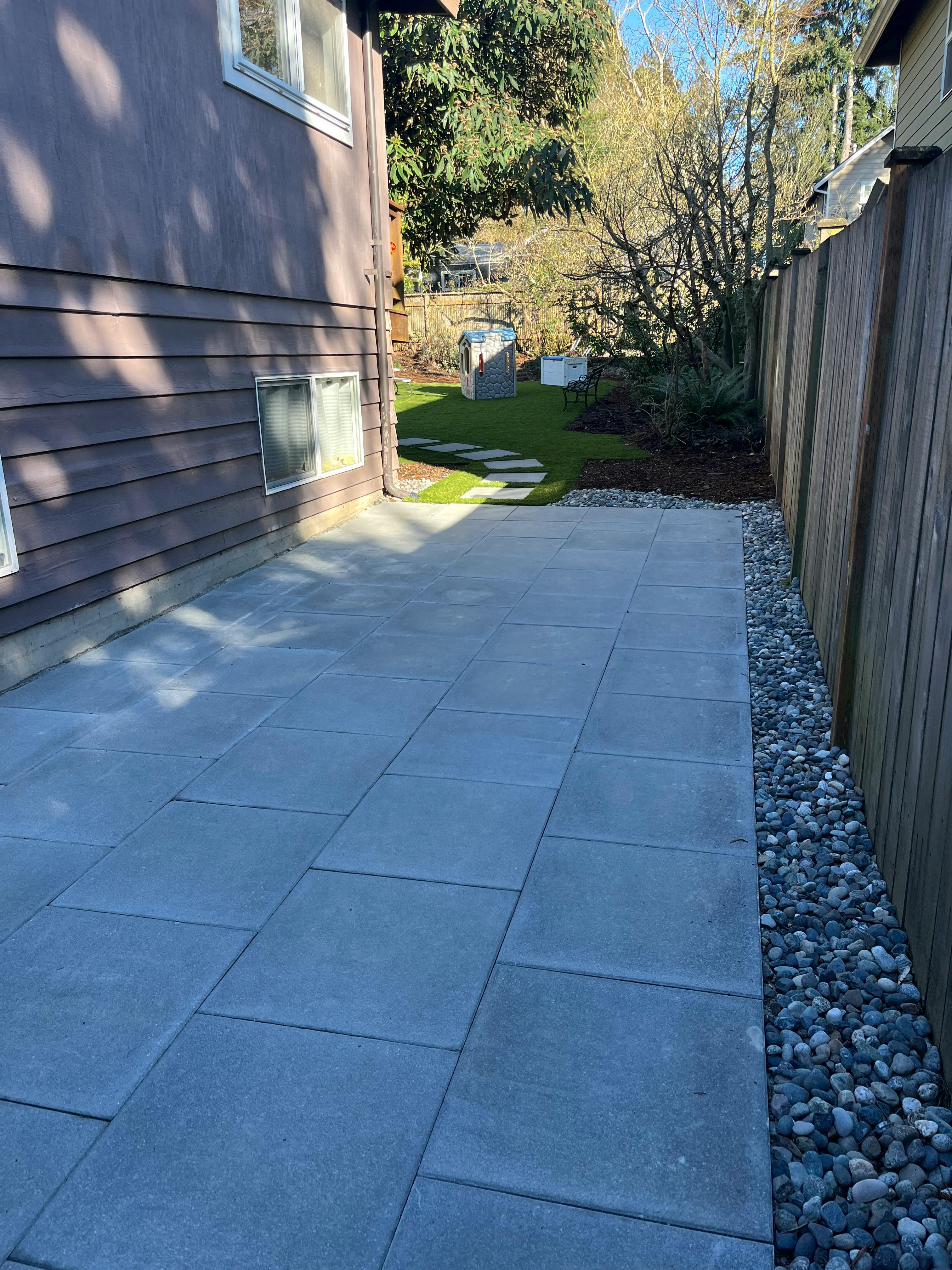 Patio with large square pavers next to a house and a wooden fence