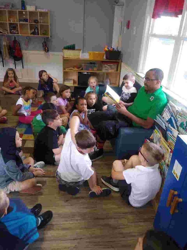 Adult reading a book to a group of children in a classroom