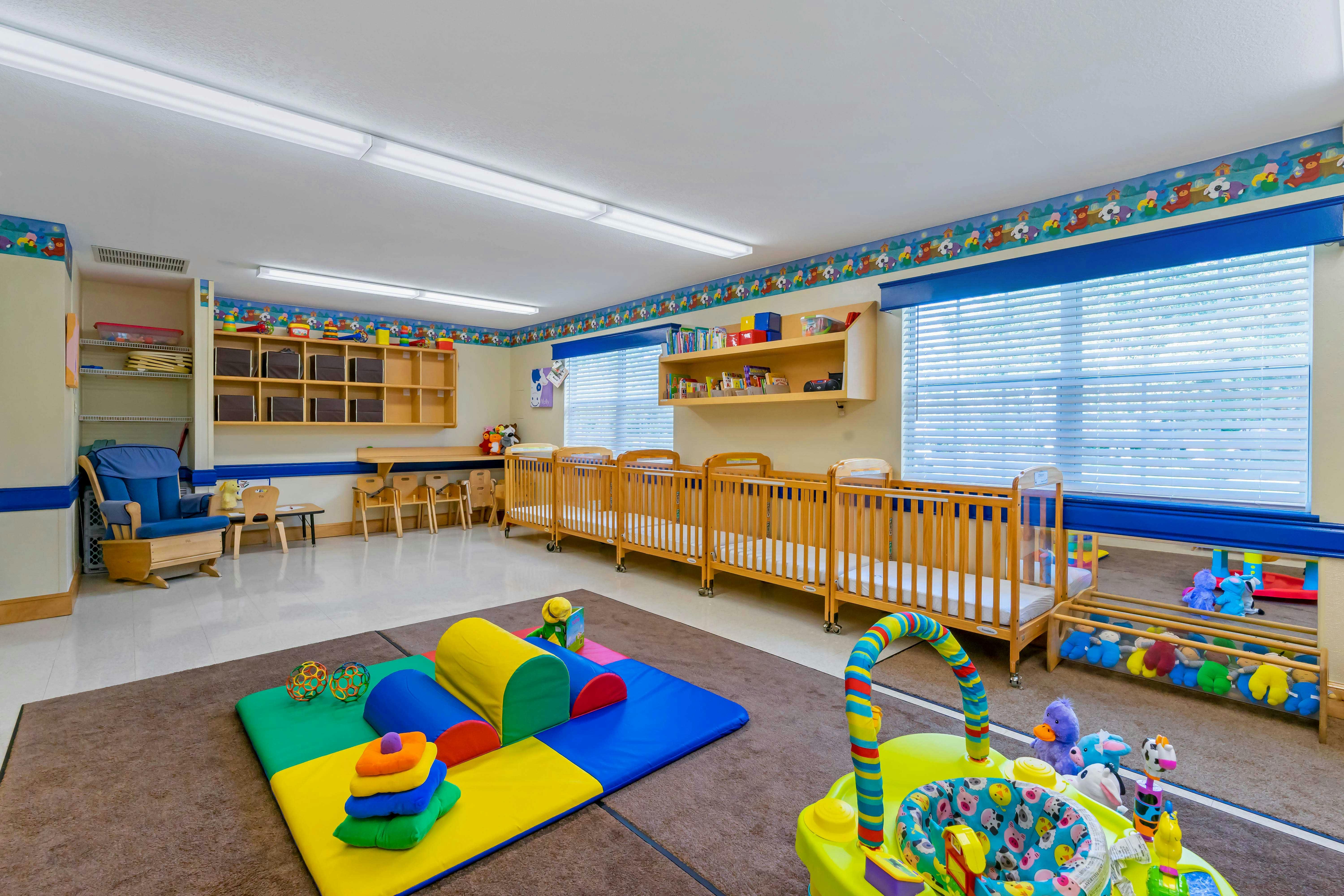 Cribs, infant play mat, rocking chair in a bright daycare room