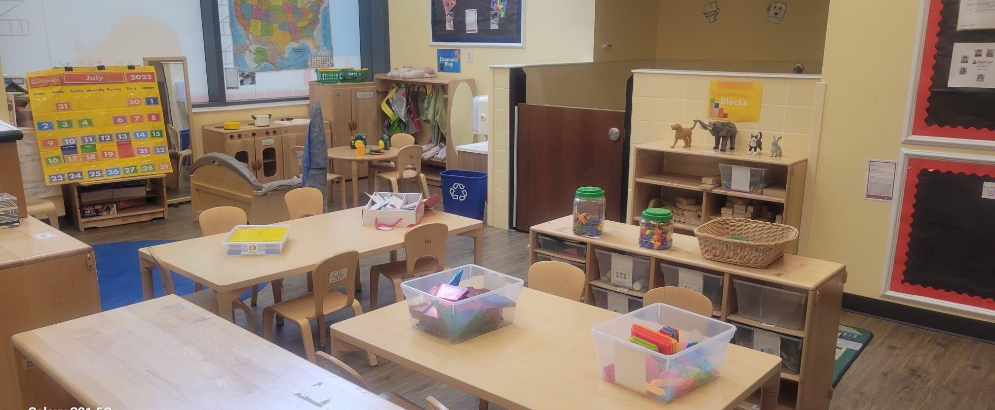 Classroom with child-sized tables and chairs, play kitchen, and toy blocks