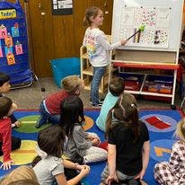 Child pointing at a whiteboard in a classroom with other children watching