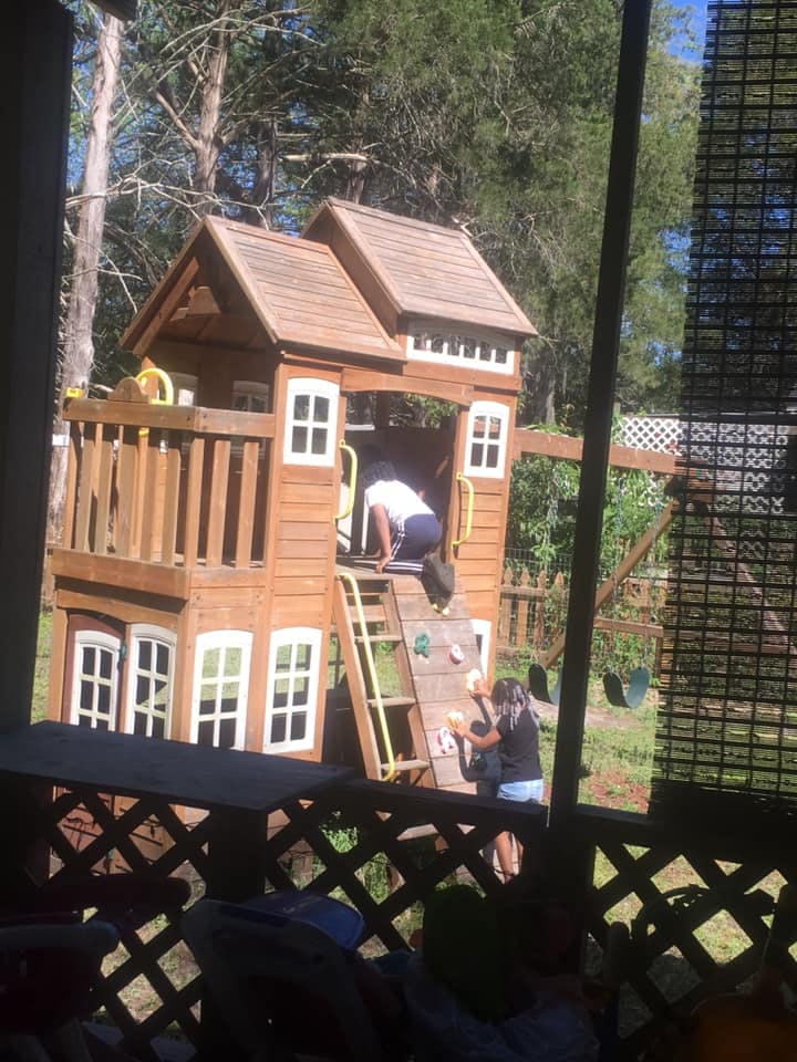 Two people on a wooden playhouse with a climbing wall
