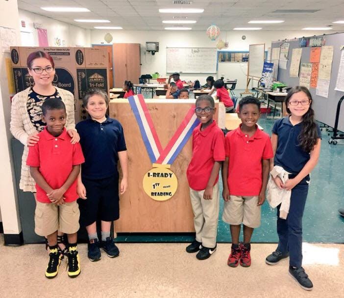 Adult and five children standing in a classroom with a large medal