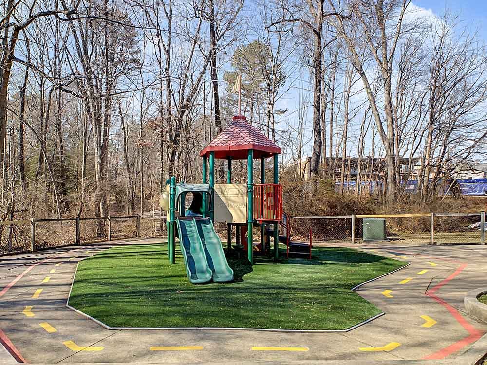 Playground structure with a slide on artificial turf surrounded by a path