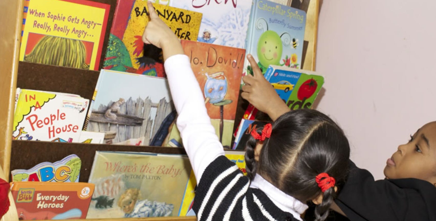 Two children reaching for books on a bookshelf