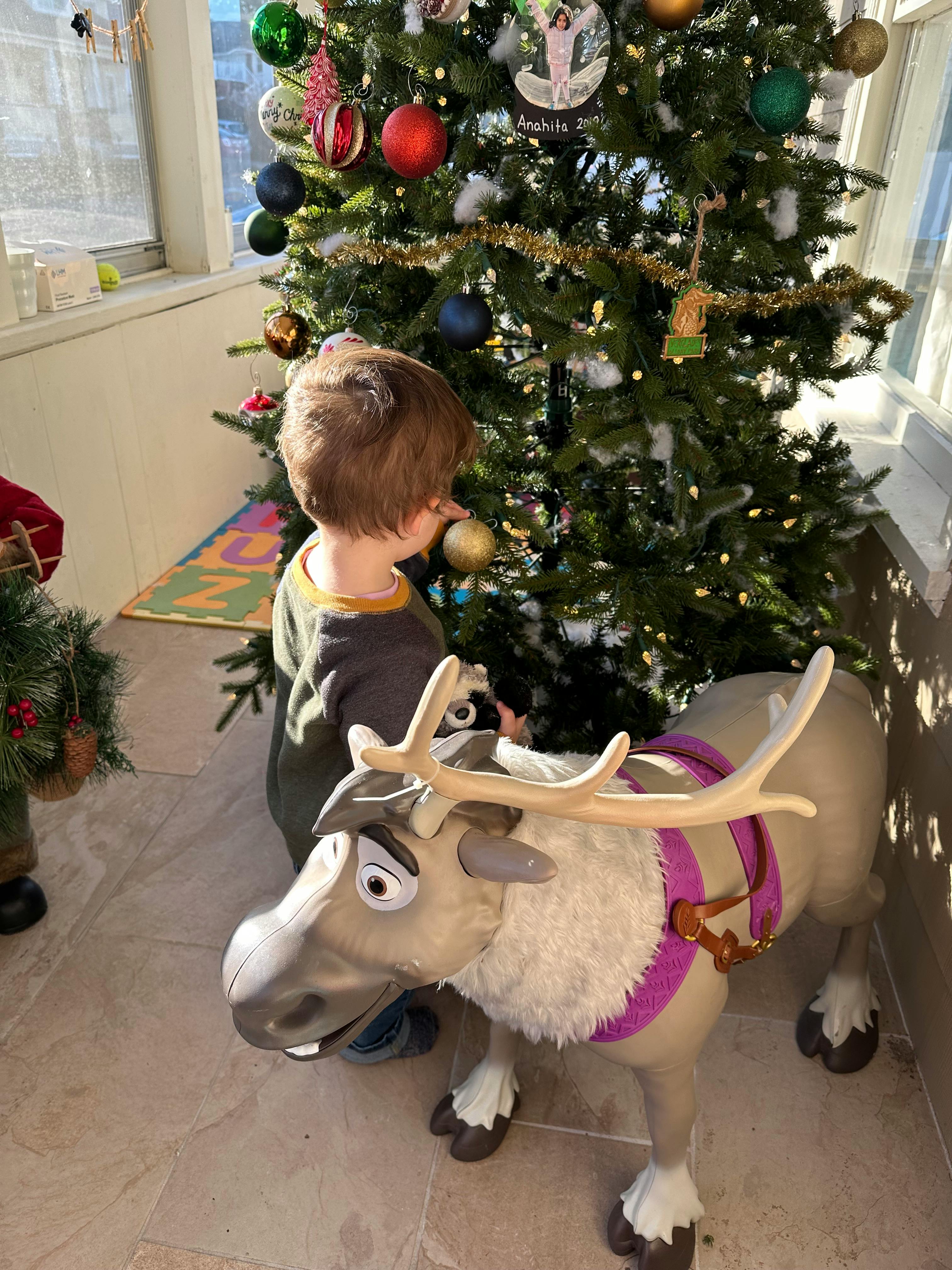 Child looking at a Christmas tree next to a reindeer toy