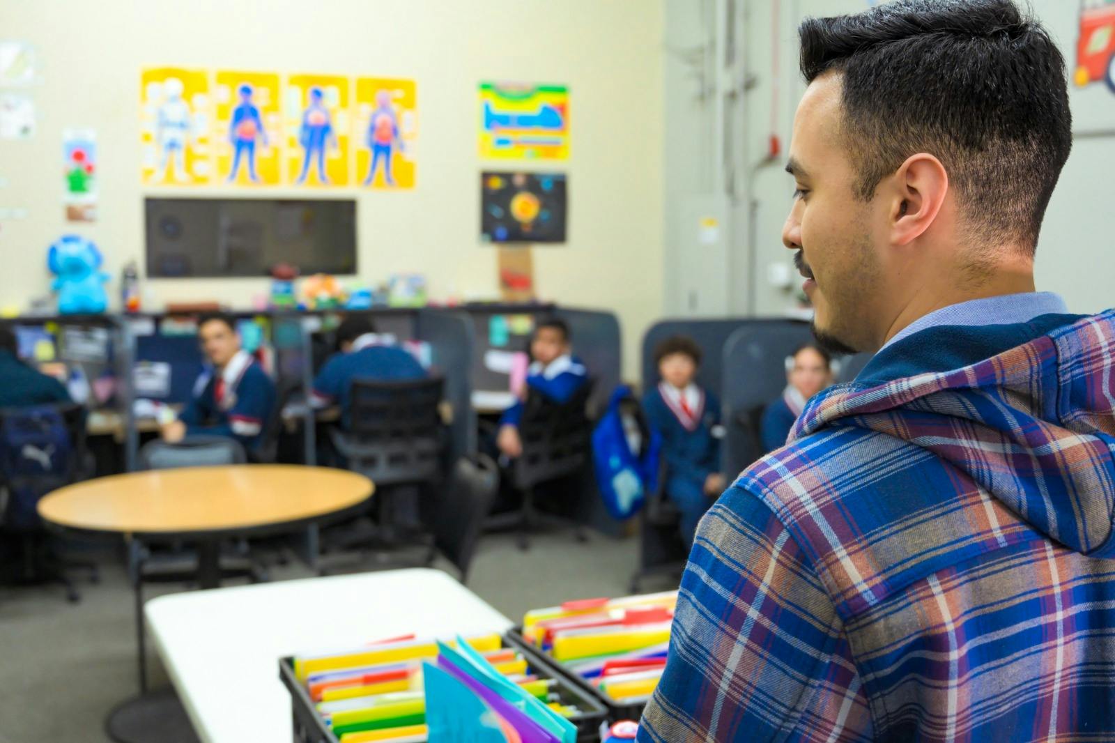 Person in plaid hoodie looking at children in a classroom