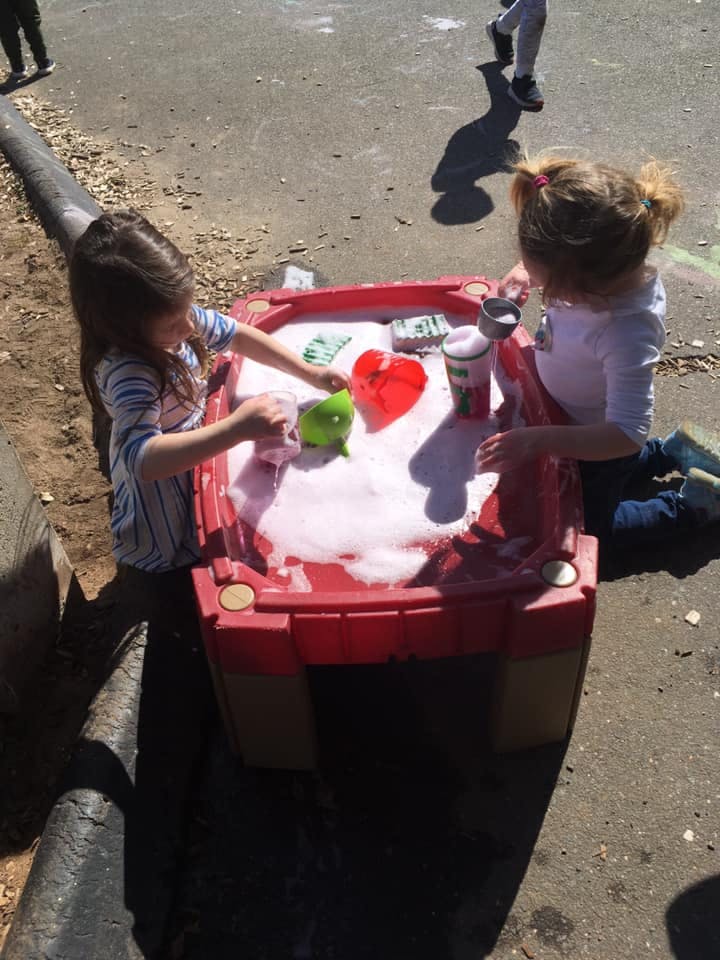 Two children playing with a red water table filled with bubbles