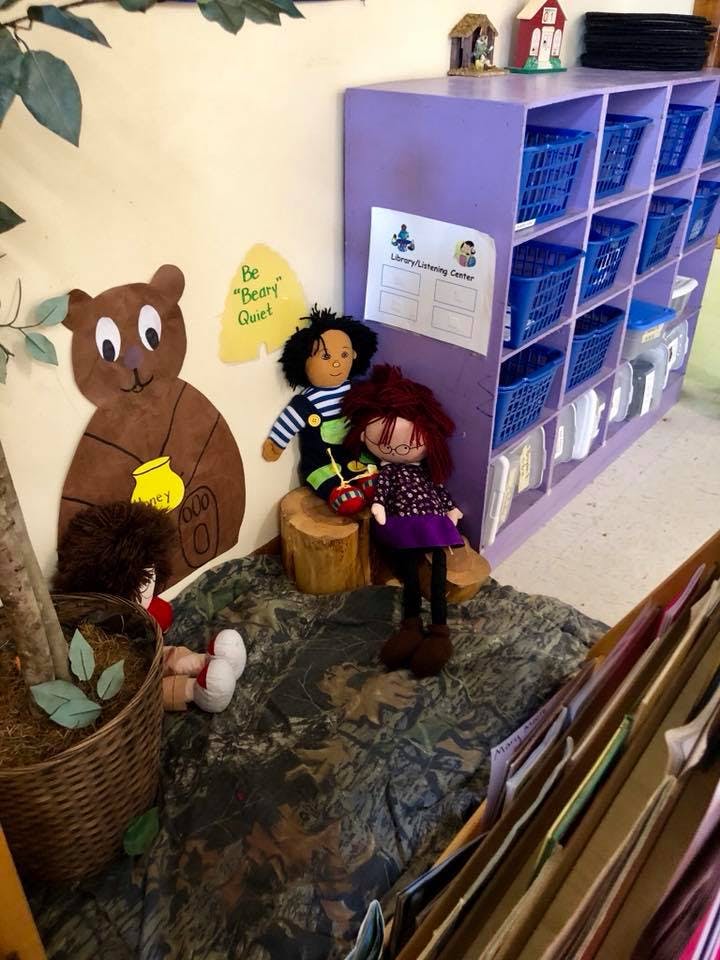 Dolls and a bear cutout in a classroom with a purple shelf