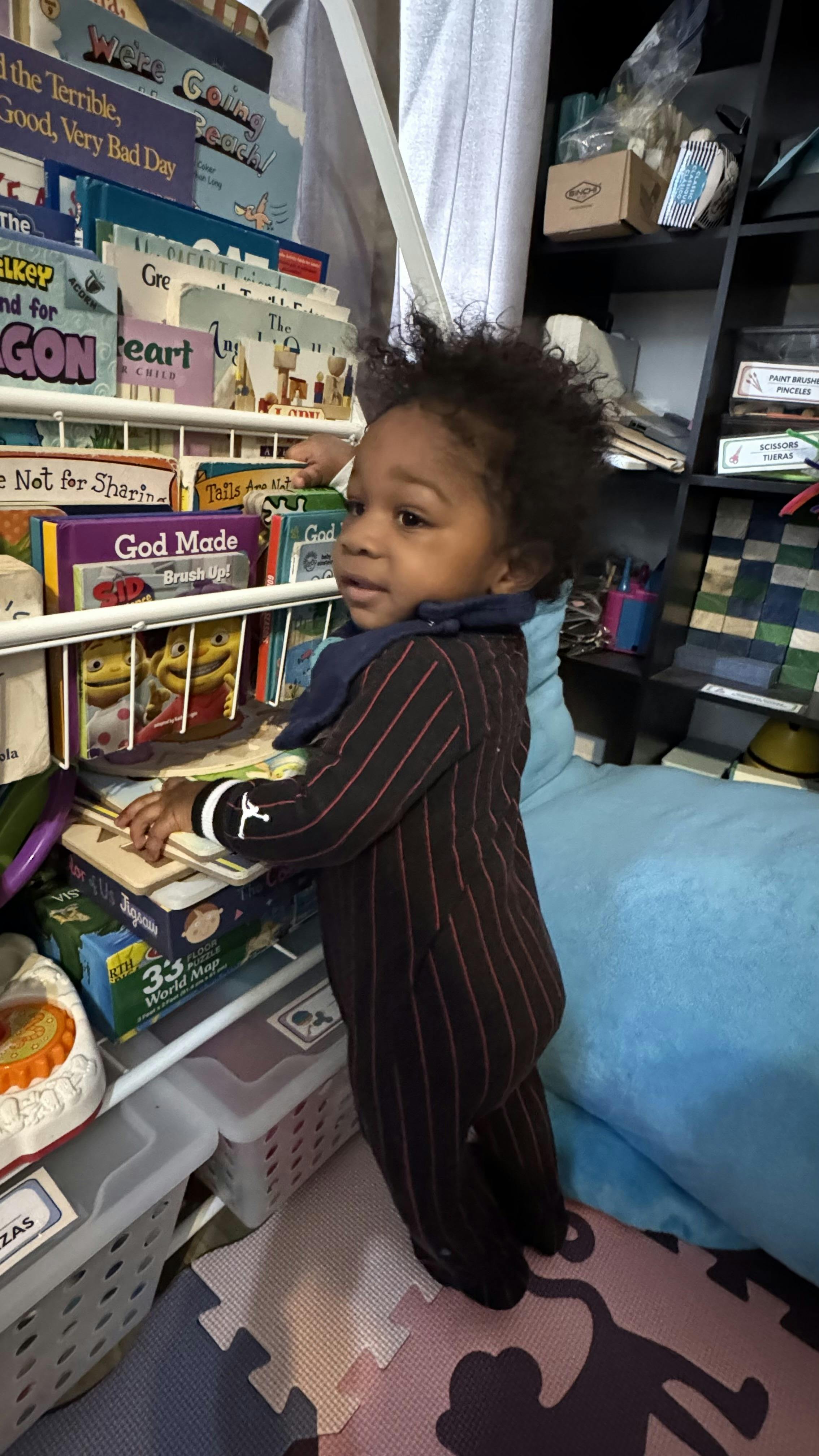 A young child standing and looking at books on a white wire shelves