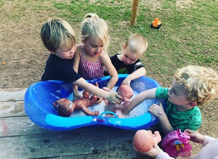 Children playing with dolls in a blue tub outdoors