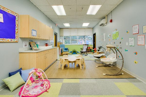 Infant classroom with small tables, chairs, and baby swings