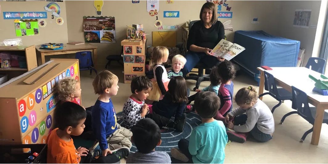 Adult reading a book to a group of children in a classroom