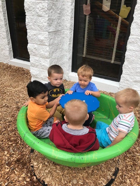 Five children playing in a green plastic sandbox