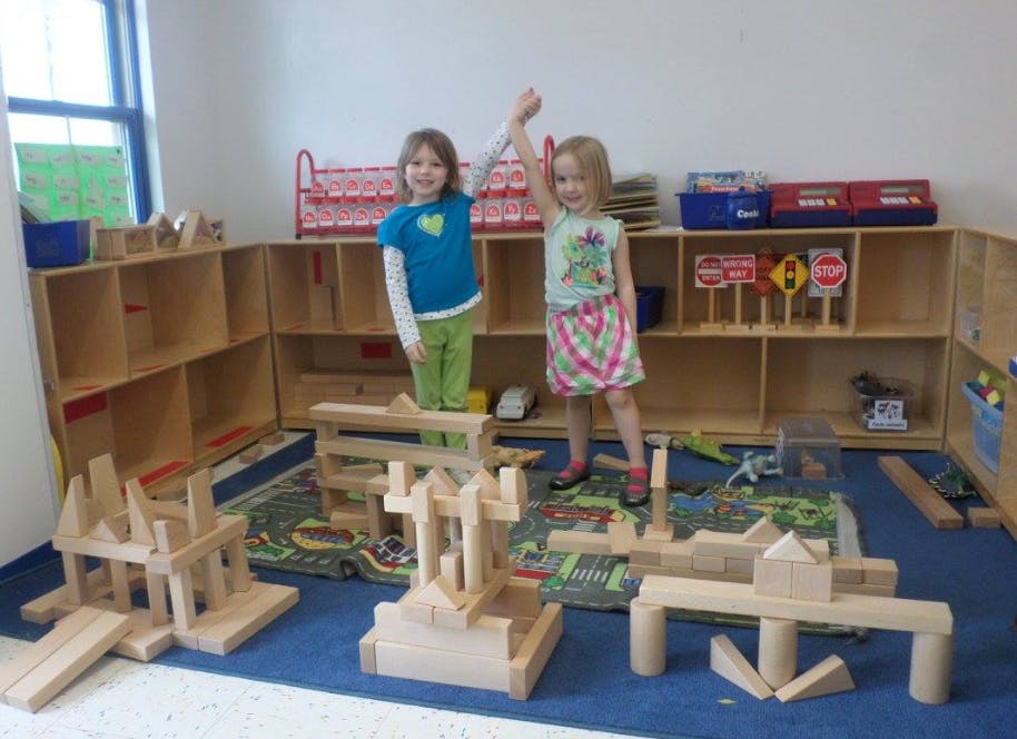 Two children standing on wooden blocks in a classroom