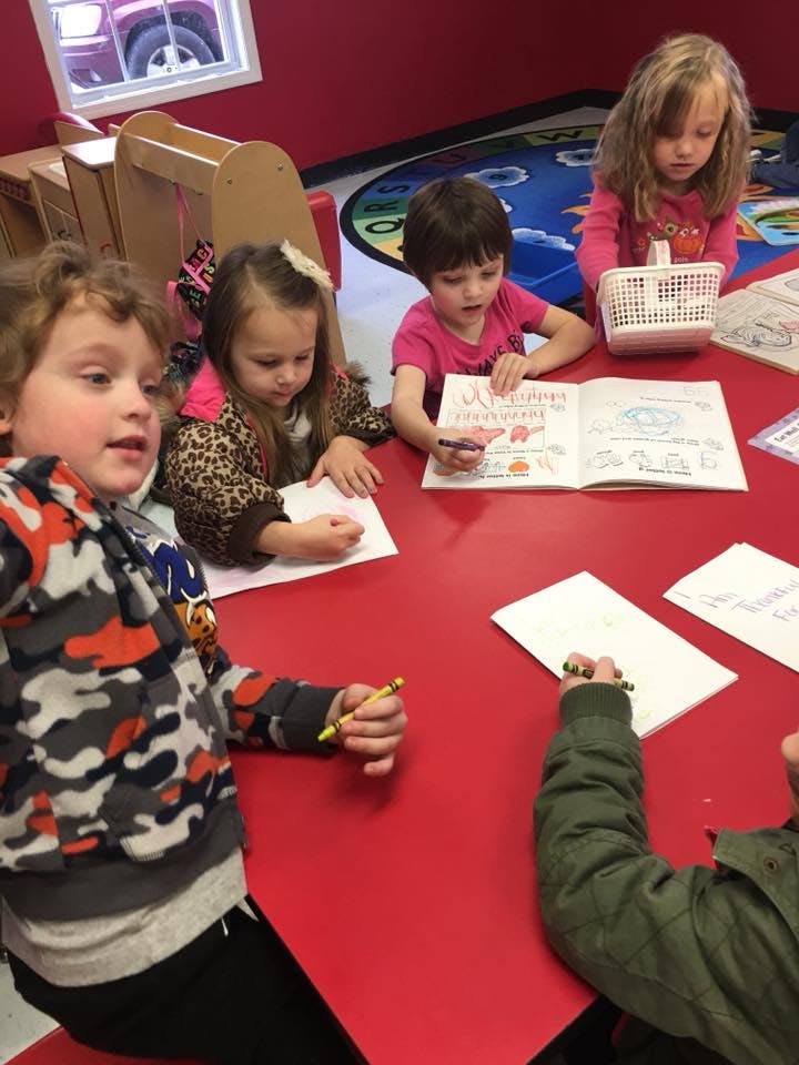 Children drawing and writing at a red table in a classroom