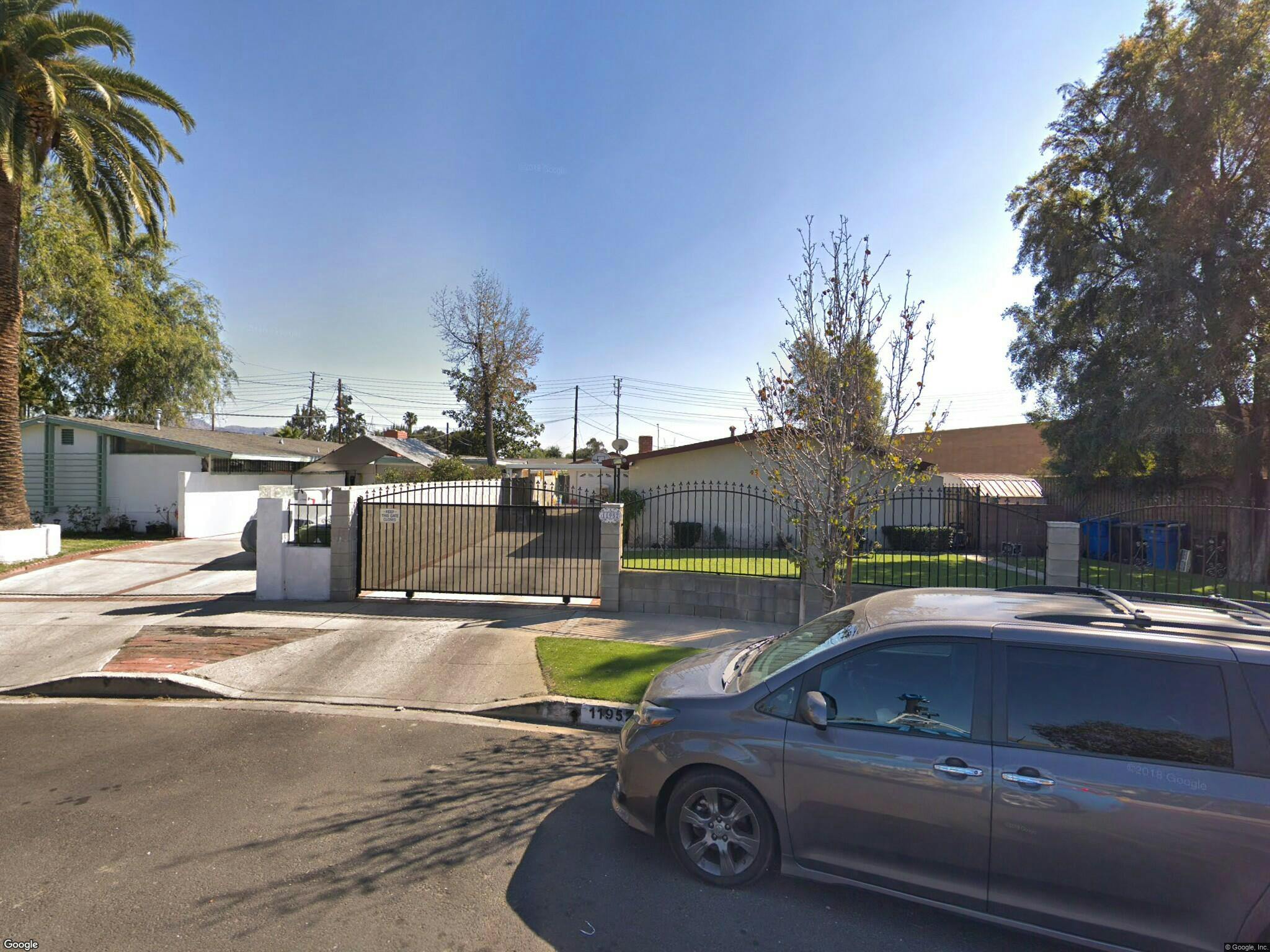 Residential street with a car parked on the right and houses behind a gate