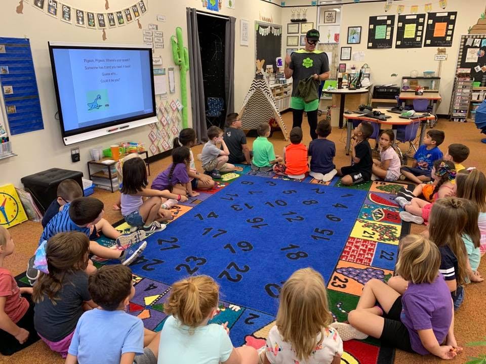 Person in costume teaching a group of children sitting on a rug in a classroom