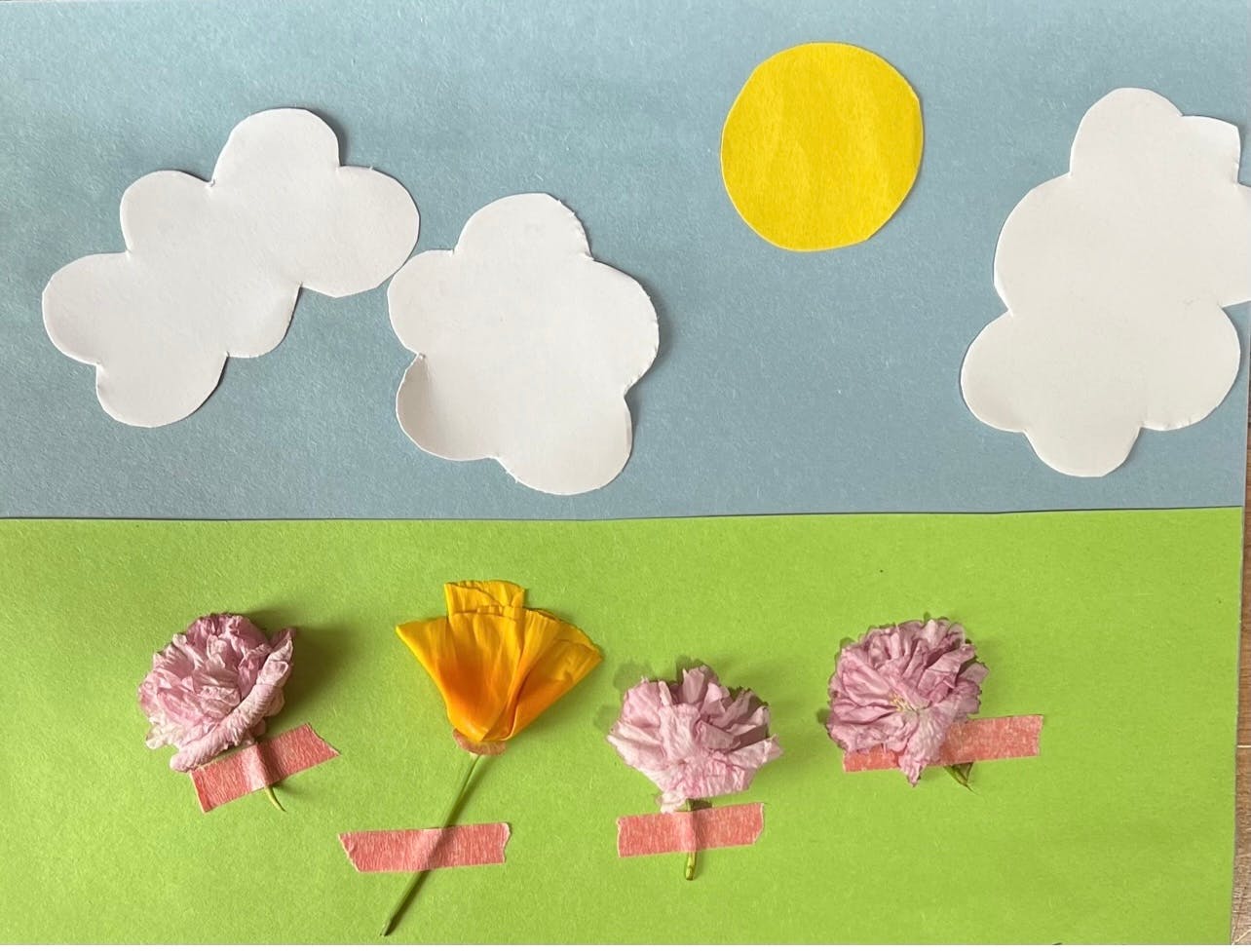 Paper cutout sun and clouds over real flowers taped to paper