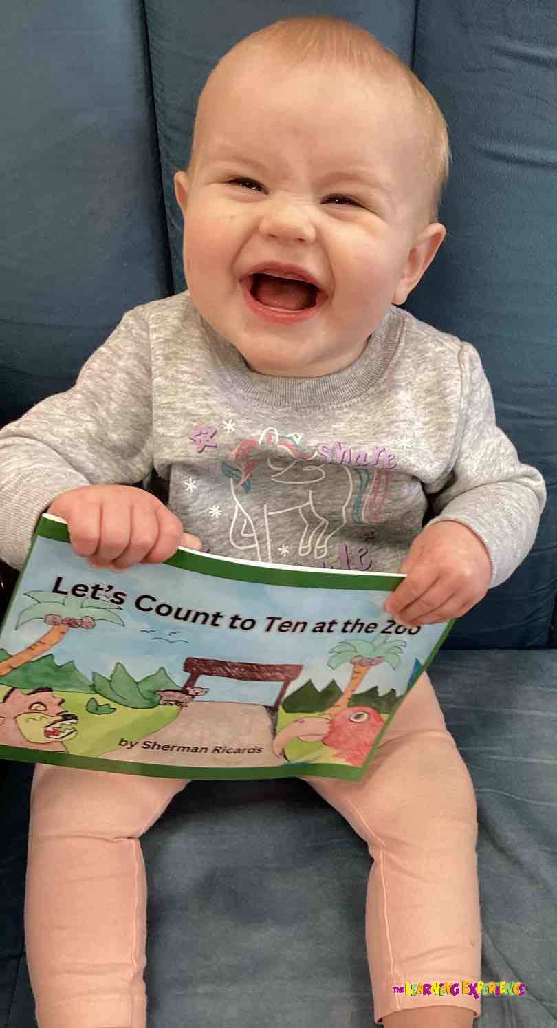 Child holding a book titled "Let's Count to Ten at the Zoo"